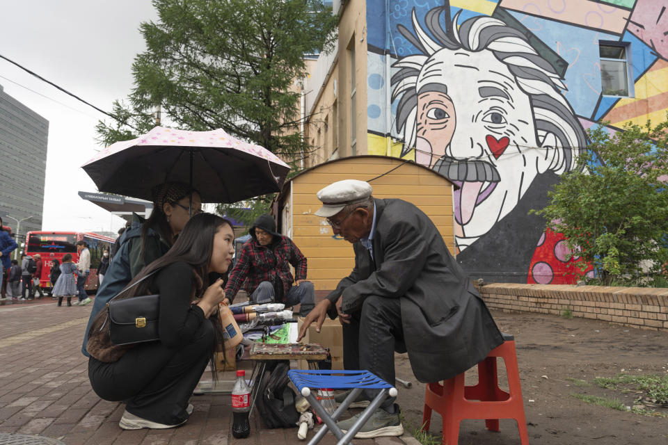 A Mongolian woman consults a fortuneteller reading fortune with stones on a street in Ulaanbaatar, Mongolia on Thursday, June 27, 2024. (AP Photo/Ng Han Guan)