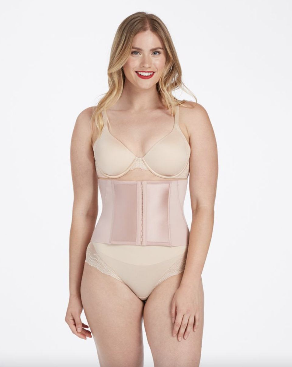 blonde model wear a light pink spanx waist cincher a beige bra and beige underwear