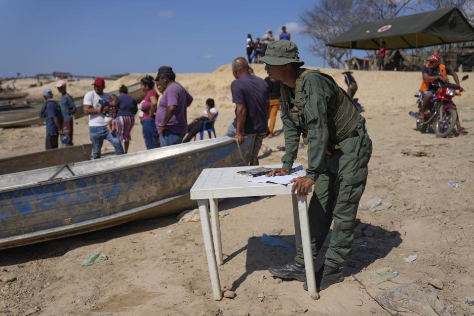 A National Guard soldier watches people arrive by boat after leaving La Bulla Loca mine, after it collapsed, in La Paragua, Bolivar state, Venezuela, Friday, Feb. 23, 2024. The collapse of the illegally operated open-pit gold mine in a remote area of central Venezuela killed at least 16 people. (AP Photo/Ariana Cubillos)