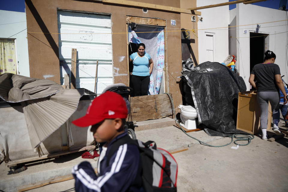 In this Jan. 28, 2020, photo, Ruth Aracely Monroy, center, looks out at her son Nahum Perla, left, as he plays in front of their home on the outskirts of Tijuana, Mexico. The Perla family of El Salvador has slipped into a daily rhythm in Mexico while they wait for the U.S. to decide if they will win asylum. A modest home has replaced the tent they lived in at a migrant shelter. (AP Photo/Gregory Bull)