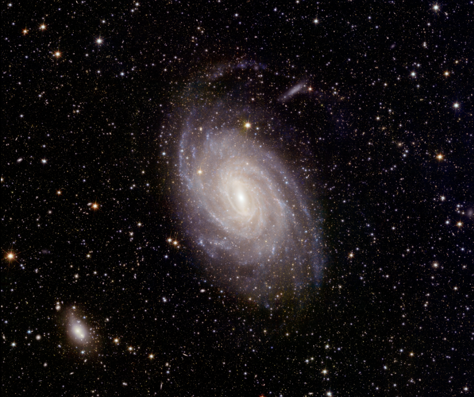 A beautiful spiral galaxy can be seen in the center of this space image.  In the background there are many stars.  A much smaller, blurry white spot in the bottom left of the scene.