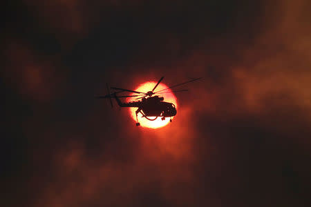 A firefighting helicopter flies in front of the setting sun as a wildfire burns near the village of Kapandriti, north of Athens, Greece, August 15, 2017. REUTERS/Alkis Konstantinidis