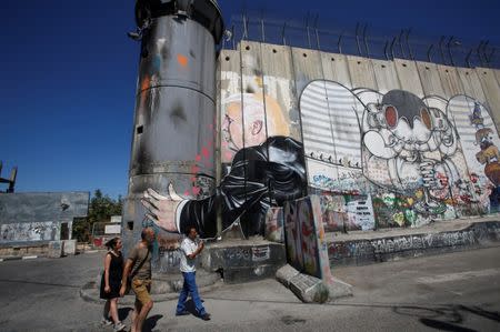 REFILE - ADDING RESTRICTIONS Tourists stand in front of a grafitti depicting U.S President Donald Trump on the controversial Israeli barrier in the West Bank town of Bethlehem August 4, 2017. REUTERS/Mussa Qawasma