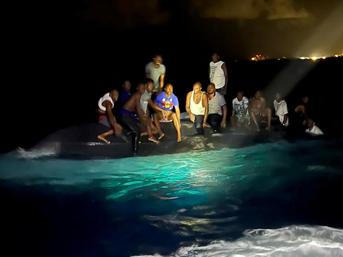 Survivors of a migrant boat that capsized perch on the overturned vessel off the coast of New Providence island (via REUTERS)