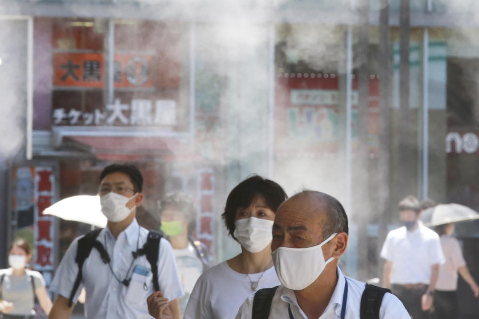 People wearing face masks to protect against the spread of the coronavirus walk under a water mist in Tokyo Thursday, Aug. 5, 2021. New cases surge in Tokyo to record levels during the Olympic Games. (AP Photo/Koji Sasahara)