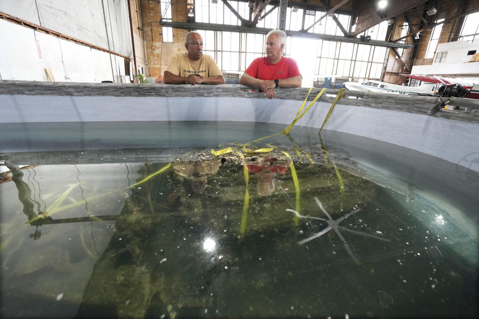 Wayne Lusardi, Michigan's state maritime archaeologist with the Department of Natural Resources, right, and Brian Smith, president and CEO of the Tuskegee Airmen National Historical Museum look over a recovered engine from a P-39 Airacobra in a chemical solution, Thursday, Aug. 17, 2023 in Detroit. The museum is working to start a capital campaign to raise funds for a new building with room to display aircraft flown by the airmen. (AP Photo/Carlos Osorio)