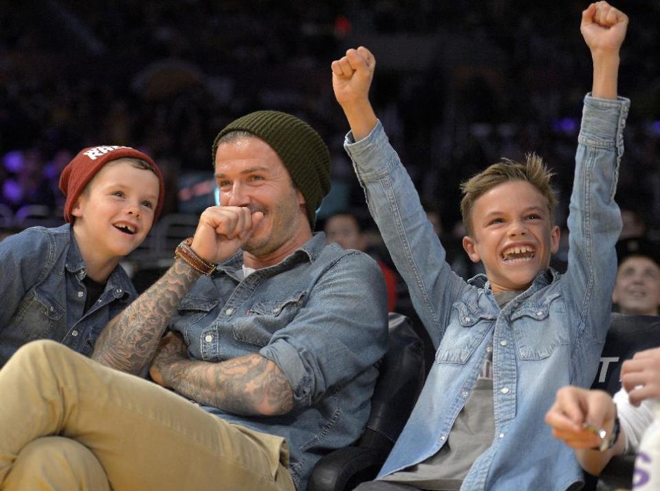 FILE- English Soccer player David Beckham, center, laughs with his sons Romeo, right, and Cruz, left, as they watch an NBA basketball game between the Los Angeles Lakers and Phoenix Suns, in this file photo dated Friday, Nov. 16, 2012, in Los Angeles, USA. It is announced Tuesday Dec. 18, 2012 that the son of soccer star David Beckham and former Spice Girl singer Victoria Beckham, ten-year old Romeo Beckham, is the new face of the London based clothing brand Burberry and features in upcoming ads for Burberry’s spring/summer 2013 collection. (AP Photo/Mark J. Terrill, file)