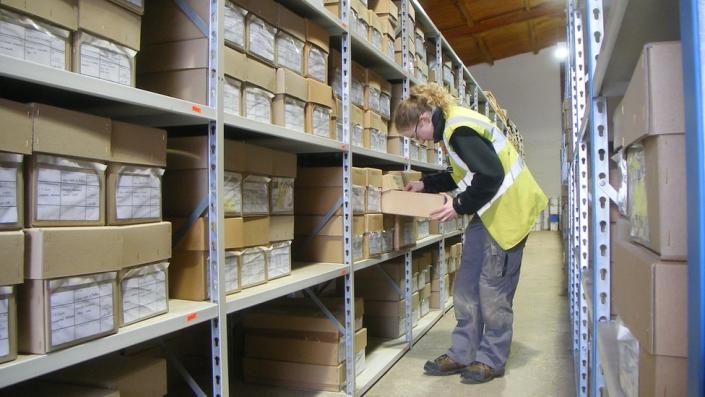 Estantes de almacenamiento con cajas con un trabajador que las atiende sosteniendo un portapapeles