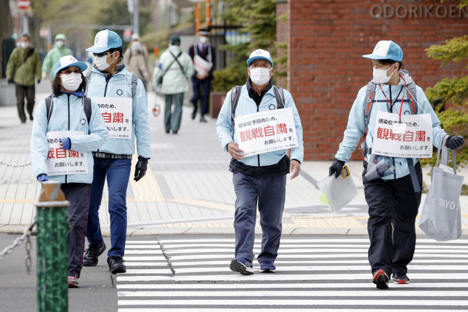 Staff walk around Odori Park with notes calling for refraining from watching a half-marathon to help curb the spread of the coronavirus in Sapporo, northern Japan, Wednesday, May 5, 2021. The half-marathon was held as a Tokyo 2020 test event three months before the Olympics open. (Hiroko Harima/Kyodo News via AP)