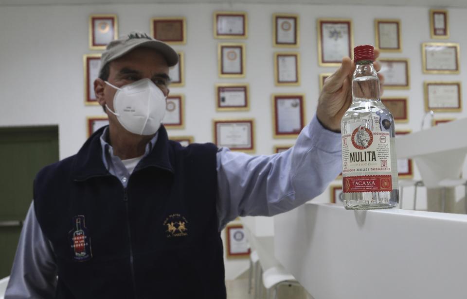 El productor de pisco José Olaechea muestra una botella de pisco de la marca La mulita en su oficina en el viñedo Tacama en Ica, Perú, el lunes 28 de septiembre de 2020. Más de 500 productores de pisco han visto caer sus ventas a la mitad y miles de agricultores han visto sus campos arruinados debido a las cosechas tardías por al estricto bloqueo implementado para detener el COVID-19. (AP Foto/Martín Mejía)