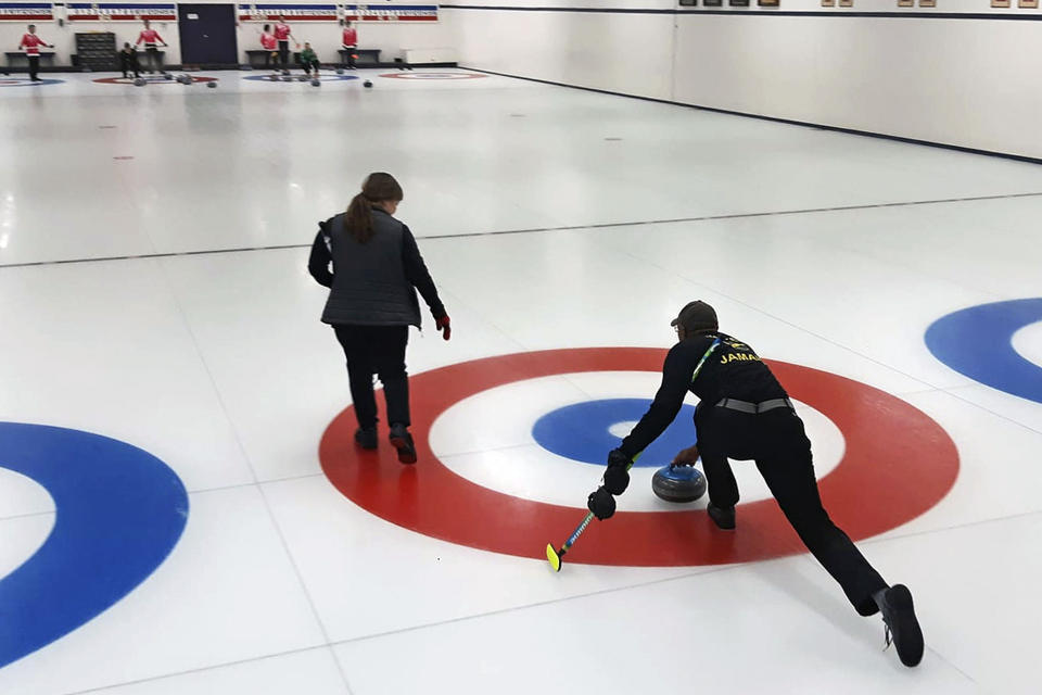 In this photo provided by Curling Jamaica, Jamaica's Andrew Walker, right, delivers a stone against Hong Kong in a practice game Saturday, Apr. 2, 2022, at the Unionville Curling Club in Markham, Ontario, Canada. The Jamaican curlers are sliding into the footsteps of the bobsledders that brought the tropical island nation to the Winter Olympics and became an international sensation. (Sandy Ewart/Curling Jamaica photo via AP)