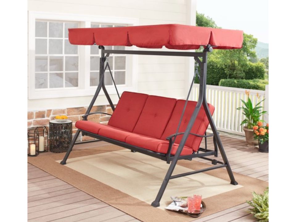 Red porch swing with cover on a backyard deck.
