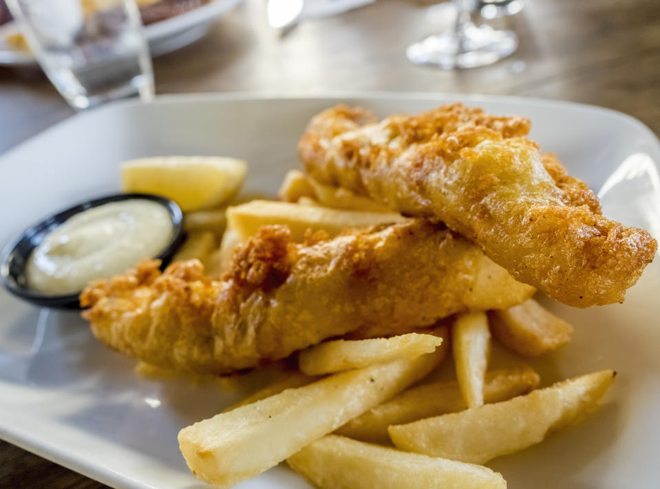 Battered fish and chips (fries) freshly cooked to golden brown, served on a plate with a wedge of lemon and some sauce.