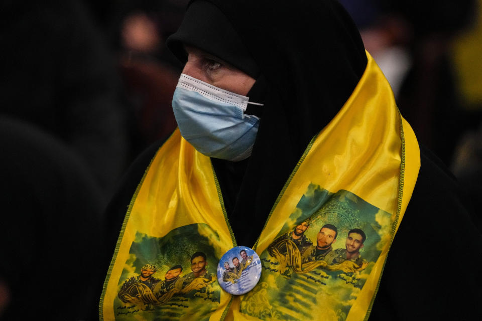 A woman wearing a scarf decorated with pictures of her three sons, who died fighting with Hezbollah against Israel and in Syria, listens to Hezbollah leader Sheik Hassan Nasrallah as he speaks via a video link, during an annual ceremony commemorating the killing of some of the Iran-backed group's top political and military leaders, in the southern suburb of Beirut, Lebanon, Wednesday, Feb. 16, 2022. Nasrallah revealed Wednesday in a televised speech that his militant faction has been manufacturing military drones in Lebanon and has the technology to turn thousands of missiles in their possession into precision-guided munitions. (AP Photo/Hassan Ammar)
