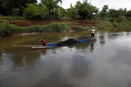 Men guide a boat carrying sand past where a section of the Citarum river is joined by a polluted tributary which runs through an area densely populated with textile factories near Majalaya, south-east of Bandung, West Java province, Indonesia, January 26, 2018. REUTERS/Darren Whiteside