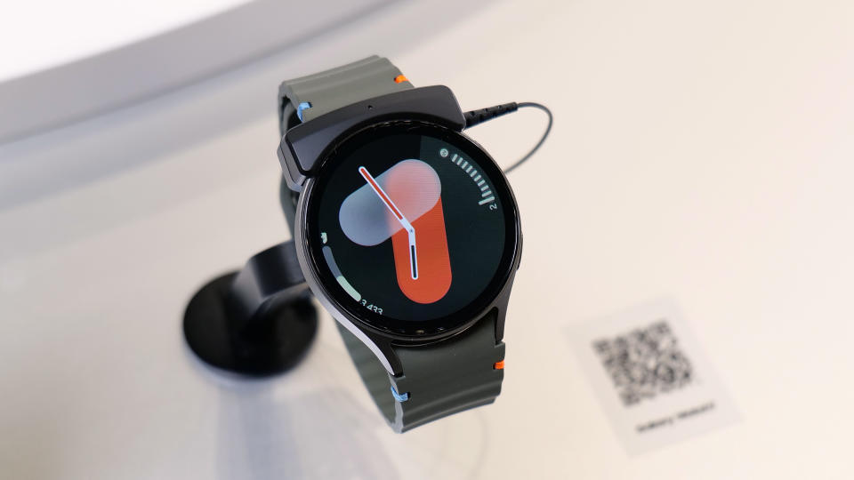 The Samsung Galaxy Watch 7 on a stand on a white table, showing an analog watch face.