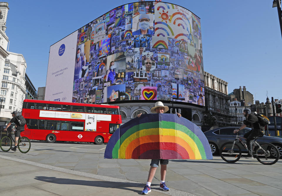 A young boy holds a painted rainbow as pictures appear on a screen during a 10 minute domination on The Piccadilly Lights, Piccadilly Circus, to mark the launch of The People's Picture interactive mosaic art project Rainbows for the NHS in London, Monday, June 22, 2020. The art installation which features thousands of photos and messages from key workers, carers, patients, doctors and nurses appears on Piccadilly Lights until June 28.(AP Photo/Frank Augstein)