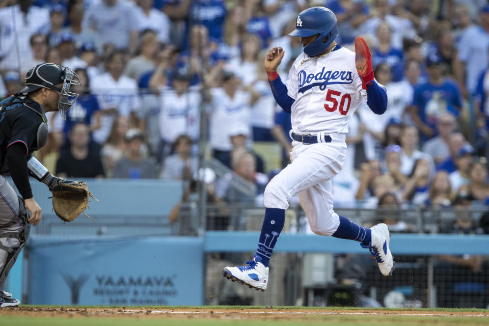 Los Angeles Dodgers' Mookie Betts, right, raises his hands to score as the throw from the outfield to Miami Marlins catcher Nick Fortes, left, is off line on an RIB single by Freddie Freeman, during the third inning of a baseball game in Los Angeles, Saturday, Aug. 20, 2022. (AP Photo/Alex Gallardo)