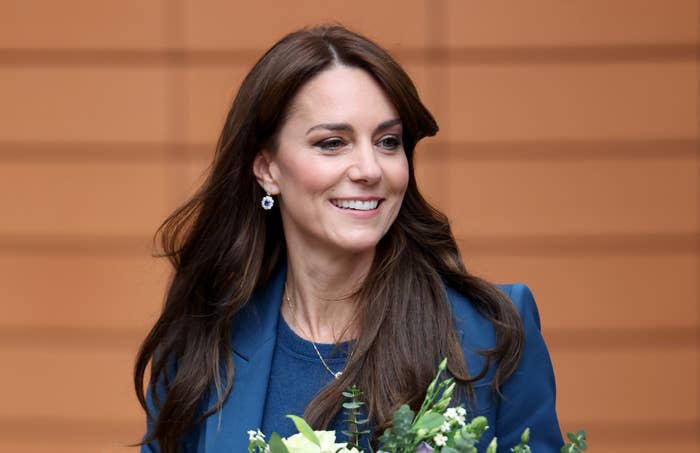 Woman smiling, holding a bouquet, wearing a dark jacket with earrings