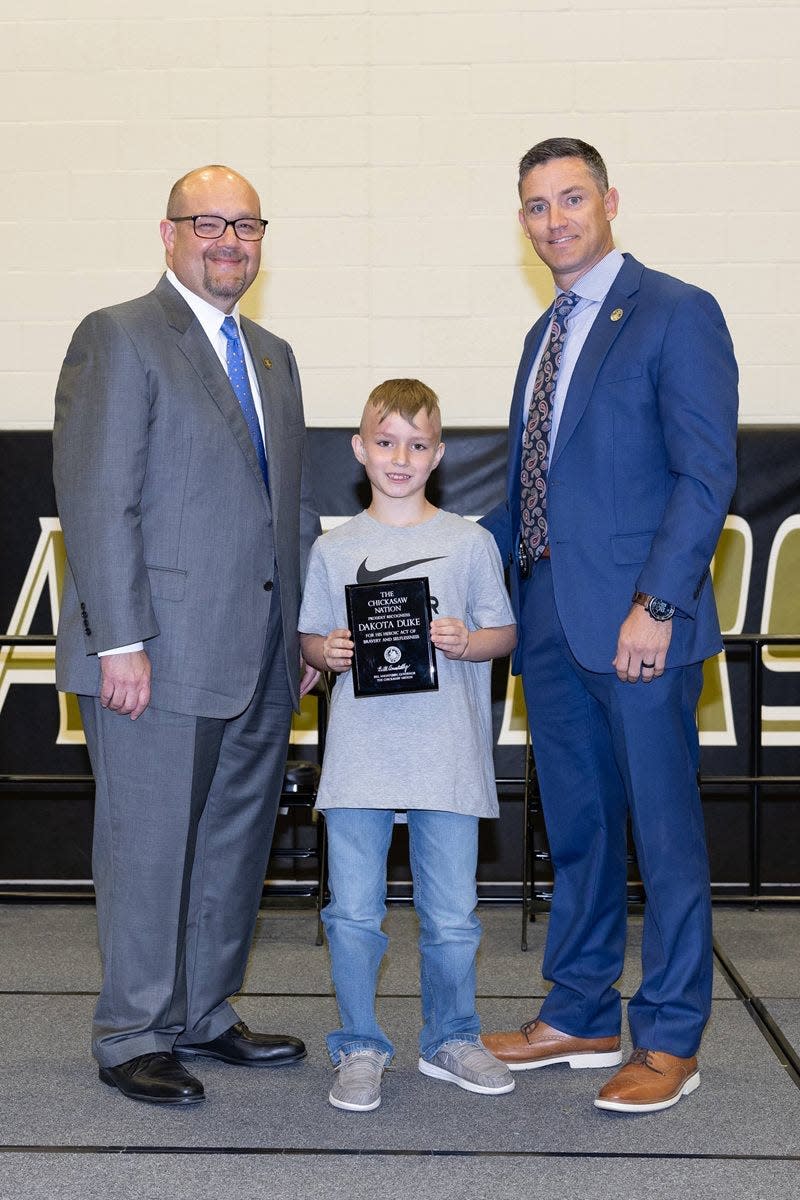 Chickasaw Nation Lt. Gov. Chris Anoatubby, left, and Lighthorse Assistant Chief Terrance Bush, right, present Dakota Duke with a plaque to recognize his heroic act of bravery and selflessness.