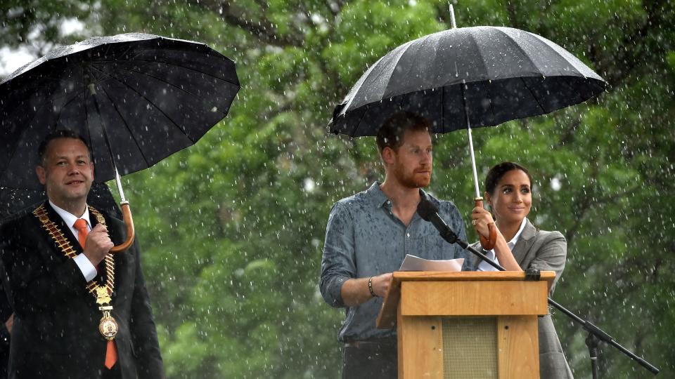 Meghan Markle holding an umbrella over Prince Harry