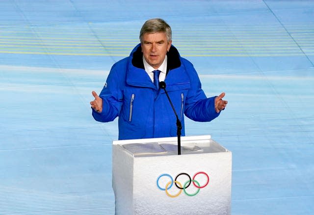 IOC president Thomas Bach, wearing a blue jacket, stands at a podium emblazoned with the Olympic rings