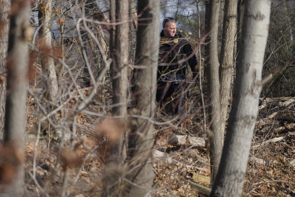 A Sayreville police officer walks through a wooded area near a townhome community, Thursday, Feb. 2, 2023, in Parlin, a section of Sayreville, N.J., where Sayreville councilwoman Eunice Dwumfour was found shot to death in an SUV parked outside her home on Wednesday. According to the Middlesex County prosecutor's office, she had been shot multiple times and was pronounced dead at the scene. (AP Photo/Seth Wenig)