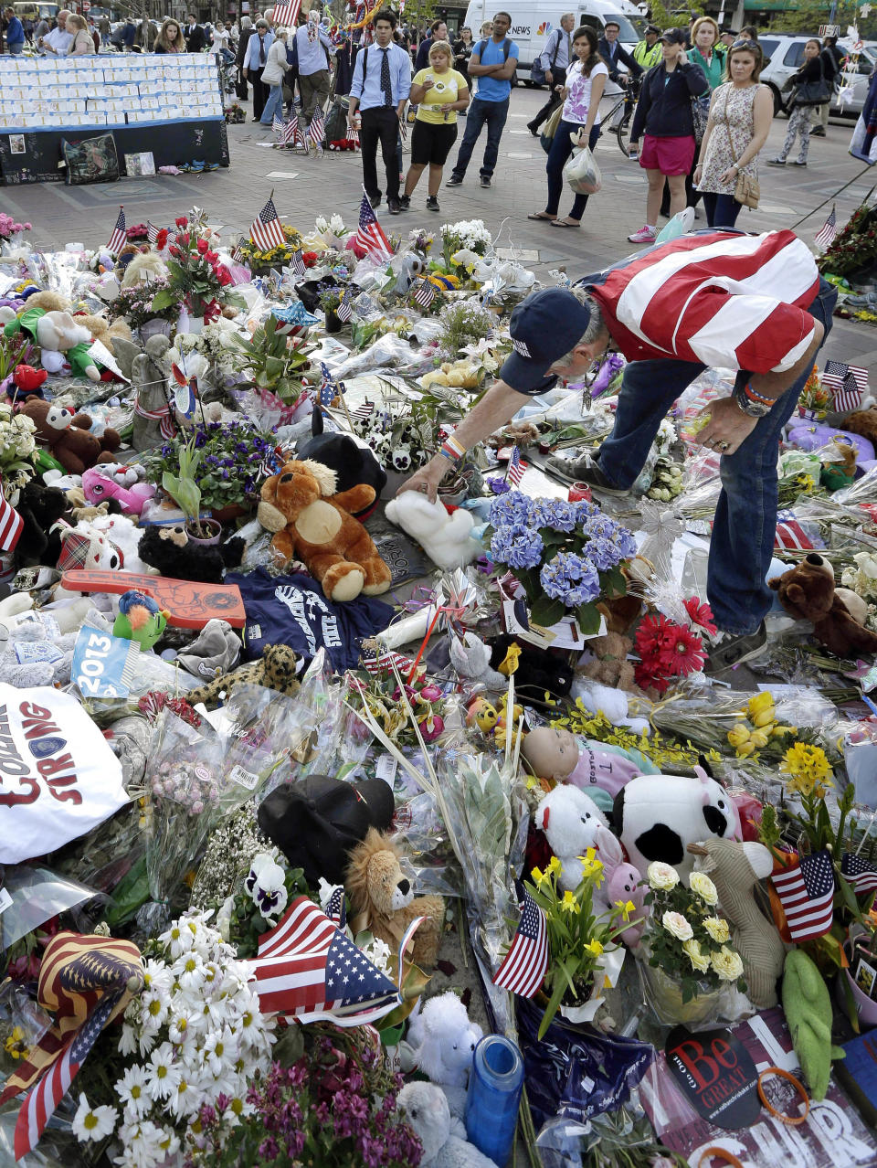 FILE - In this May 7, 2013 file photo, Kevin Brown, of Boston, right, places a Teddy bear at a makeshift memorial to the victims of the April 15 bombings near the Boston Marathon finish line in Boston's Copley Square. Thousands of items from the original memorial for marathon bombing victims are going on display at the Boston Public Library in April 2014 to mark the anniversary of the attacks. (AP Photo/Steven Senne, File)