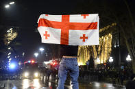 A protester holds a Georgian national flag standing in front of a police line outside the Georgian parliament building in Tbilisi, Georgia, Thursday, March 9, 2023. Police in Georgia's capital have fired water cannons and tear-gas to disperse demonstrators around the parliament building protesting a draft law aimed at curbing the influence of "foreign agents," among fears it could be used to silence opposition. (AP Photo)