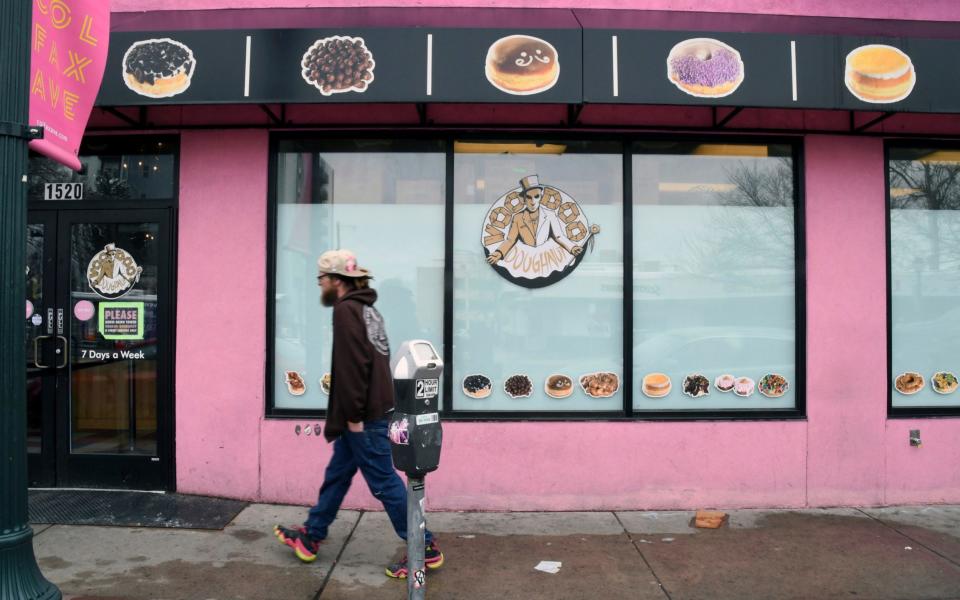 A man walks past the storefront of Voodoo Doughnut in Denver - Credit: AP