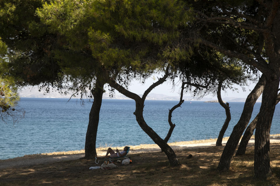 A man reads a book as he lies on a sun bed under pines at Varkiza village, a few miles southwest of Athens, on Thursday, July 29, 2021. One of the most severe heat waves recorded since 1980s scorched southeast Europe on Thursday, sending residents flocking to the coast, public fountains and air-conditioned locations to find some relief, with temperatures rose above 40 C (104 F) in parts of Greece and across much of the region. (AP Photo/Yorgos Karahalis)