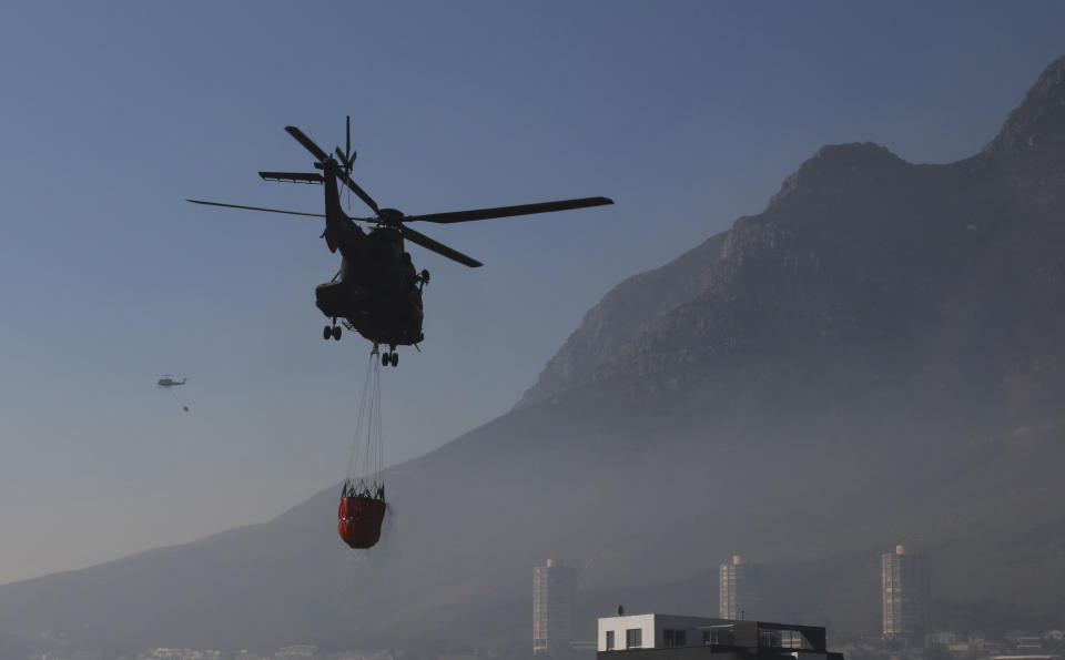 Water bombing helicopters hover by the slopes of Cape Town's, Table Mountain slopes, in South Africa, Tuesday, April 20, 2021. Fire crews worked for a third day to extinguish a wildfire as the city came to terms with the damage caused by what officials have described as one of the area's worst blazes in years. (AP Photo/Nardus Engelbrecht)