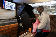 FILE - In this Oct. 27, 2020, file photo, Ron Williams, Jr., of Washington, has his daughter Mimi Williams, 2, help him to push the button while casting his vote at an early voting center at Nationals Park in Washington. Several years since its founding, BLM has evolved well beyond the initial aspirations of its early supporters. Now, its influence faces a test, as voters in the Tuesday, Nov. 3 general election choose or reject candidates who endorsed or denounced the BLM movement amid a national reckoning on race. (AP Photo/Jacquelyn Martin, File)