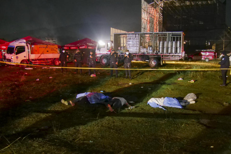 Firefighters and police stand next to the bodies of people who died in a stampede during an outdoor concert for Independence Day celebrations in Quetzaltenango, Guatemala, early Thursday, Sept. 15, 2022. According to firefighters, at least nine people died and another 20 were injured in a crush of people who were trying to enter an outdoor music concert. (AP Photo/Gustavo Rodas)