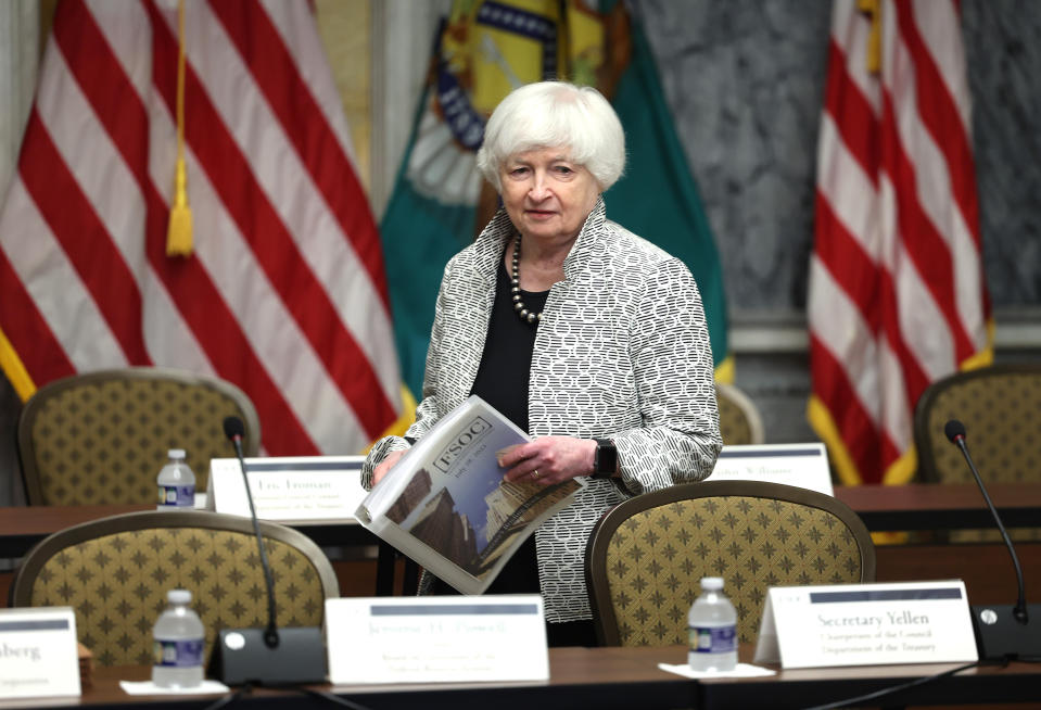 US Treasury Secretary Janet Yellen arrives for a meeting carrying a binder with American flags in the background.