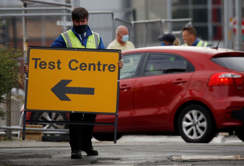 FILE PHOTO: A worker carries an information sign as a coronavirus disease (COVID-19) drive-through testing facility is opened in Bolton, Britain