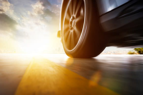 Close-up of a car's front left tire in motion next to a yellow line in the road