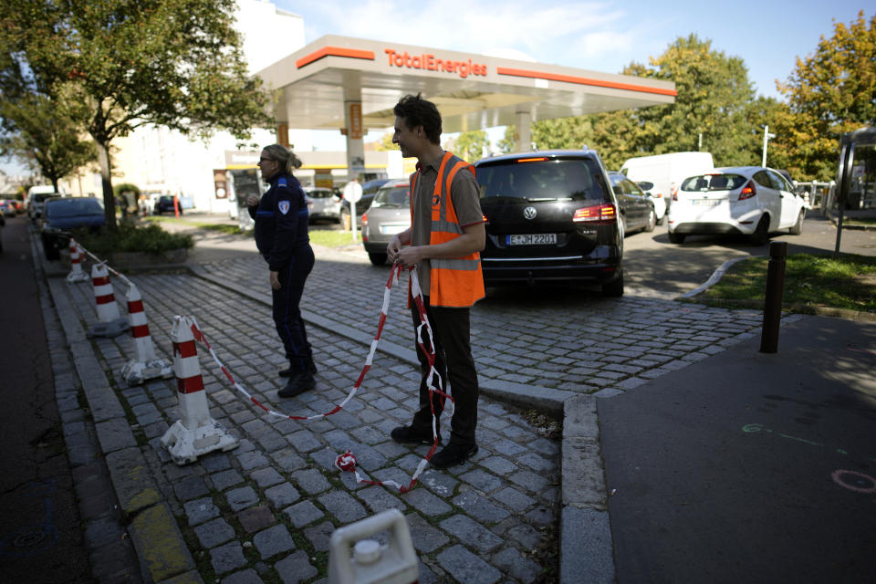 A gas station worker and a police officer set up a ribbon as they close a gas station in Paris, October 11, 2022, amid supply shortages caused largely by strikes that have hit French fuel refineries. / Credit: Christophe Ena/AP