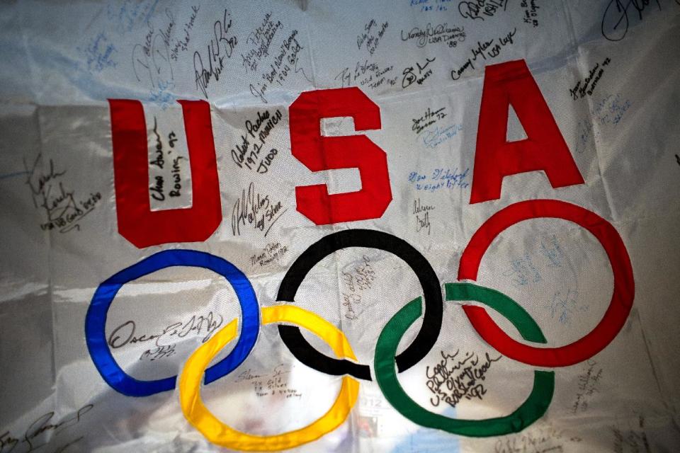 Light shines on a flag with the signatures of athletes taking part at the 2012 Summer Olympics, Wednesday, Aug. 8, 2012, in London.. London has been issuing stamps every day with photos of Britain’s gold medallists. (AP Photo/Emilio Morenatti)