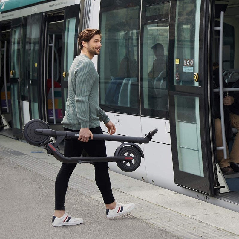 Man in leisure wear carrying a folded down Segway scooter while boarding subway train.