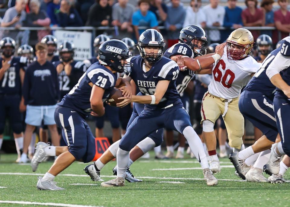 Exeter quarterback Evan Pafford hands the ball off to running back Bradley Richards as Ryan Graney (88) fends off Portsmouth's Cameron Worster in the season opener.