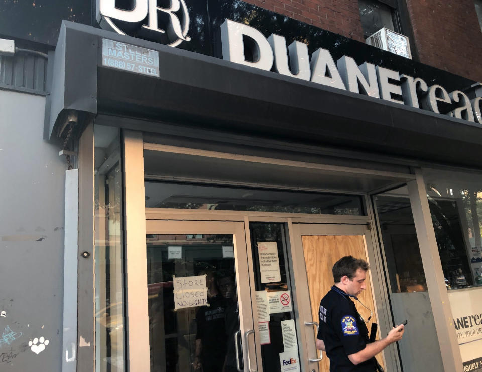 A New York State Emergency Medical Technician looks at his mobile phone while standing in front of a Duane Reade store that closed after loosing power, Saturday, July 13, 2019, in New York. Authorities were scrambling to restore electricity to Manhattan following a power outage that knocked out Times Square's towering electronic screens and darkened marquees in the theater district and left businesses without electricity, elevators stuck and subway cars stalled. (AP Photo/Leezel Tanglao)