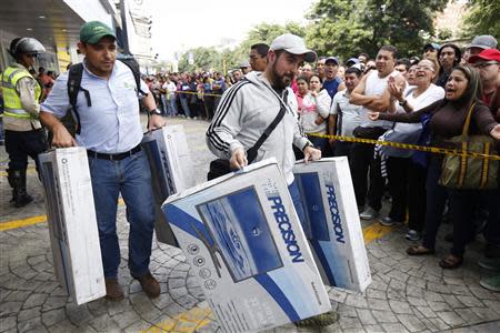 Shoppers carry electronic goods outside a Daka store in Caracas November 9, 2013. REUTERS/Carlos Garcia Rawlins