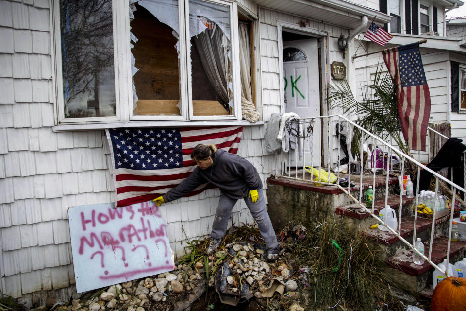 File-This photo from Friday, Nov. 2, 2012, shows Sandra Finnegan at her brother's house in Staten Island, N.Y., which was destroyed Superstorm Storm Sandy, placing a sign aimed at Mayor Michael Bloomberg for allowing the New York marathon as the city suffered. The storm killed 44 people and plunged swaths of the city into darkness, flooding tens of thousands of homes, swamped subways and forced evacuations of hospitals and nursing homes. (AP Photo/Seth Wenig, File)