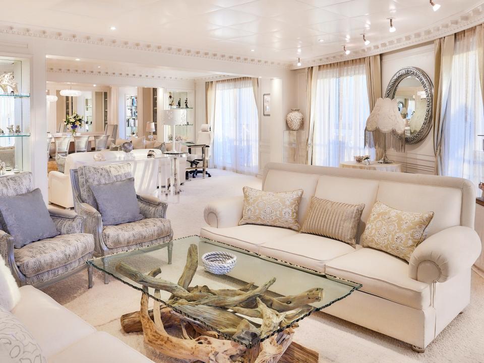 A stateroom inside The World with a white and cream-coloured interior, a seating area, and large windows.