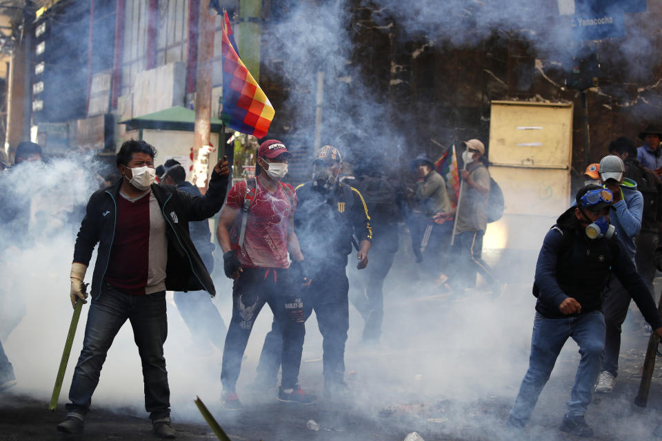A supporter of former President Evo Morales stands holding a Wiphala flag, in clouds of tear gas during clashes with police in La Paz, Bolivia, Friday, Nov. 15, 2019. Morales stepped down on Sunday following nationwide protests over suspected vote-rigging in an Oct. 20 election in which he claimed to have won a fourth term in office. An Organization of American States audit of the vote found widespread irregularities. (AP Photo/Natacha Pisarenko)