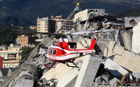  A helicopter hovers as rescuers work at the site where the Morandi motorway bridge collapsed in Genoa - Credit: AFP