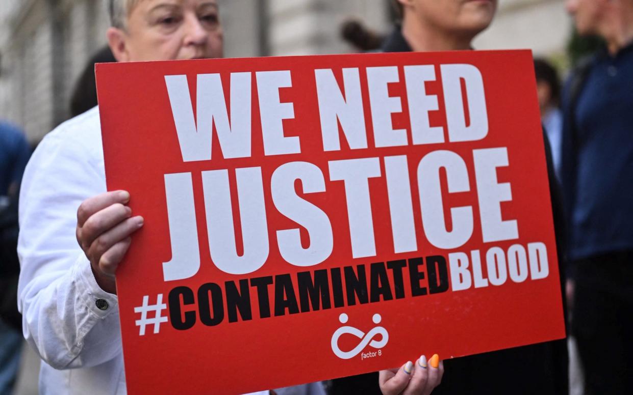 Demonstrators hold placards reading message related to the NHS infected blood scandal