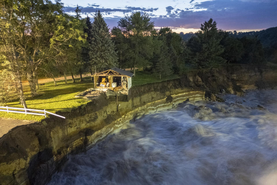 This long-exposure drone photo provided by AW Aerial shows a home as it teeters before partially collapsing into the Blue Earth River at the Rapidan Dam in Rapidan, Minn., Tuesday, June 25, 2024. (Andrew Weinzierl/AW Aerial via AP)