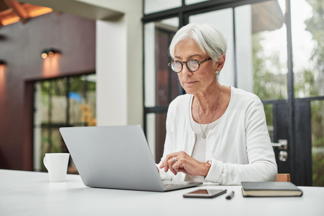 White-haired woman with glasses using laptop. 
